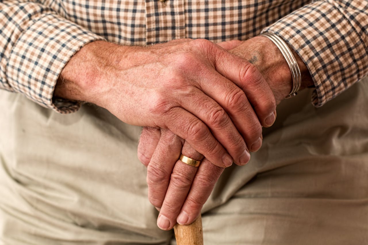 gallery-01 A detailed image of elderly hands clasping a wooden cane, symbolizing aging and support.