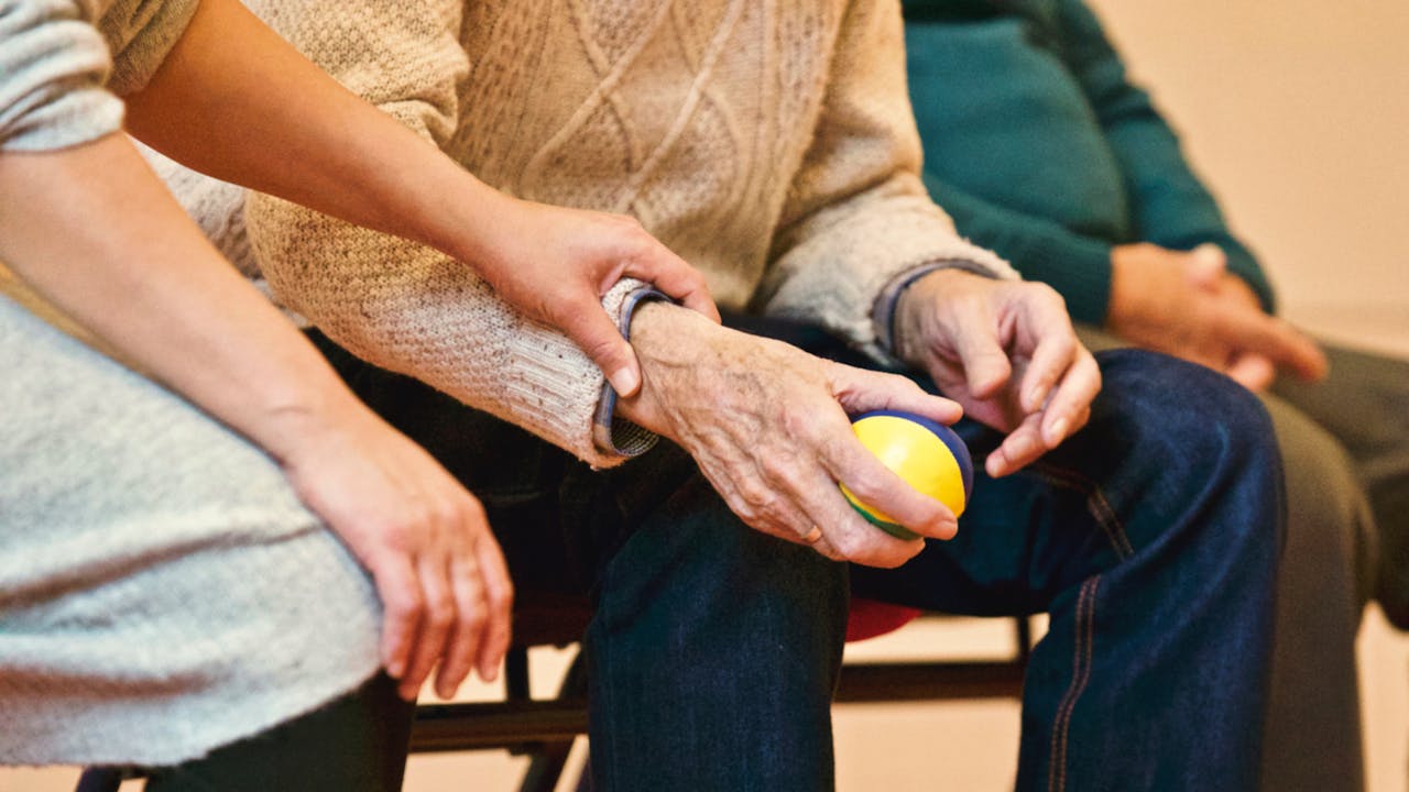 gallery-02 An elderly person receives support from a caregiver, holding hands indoors, showcasing compassion.
