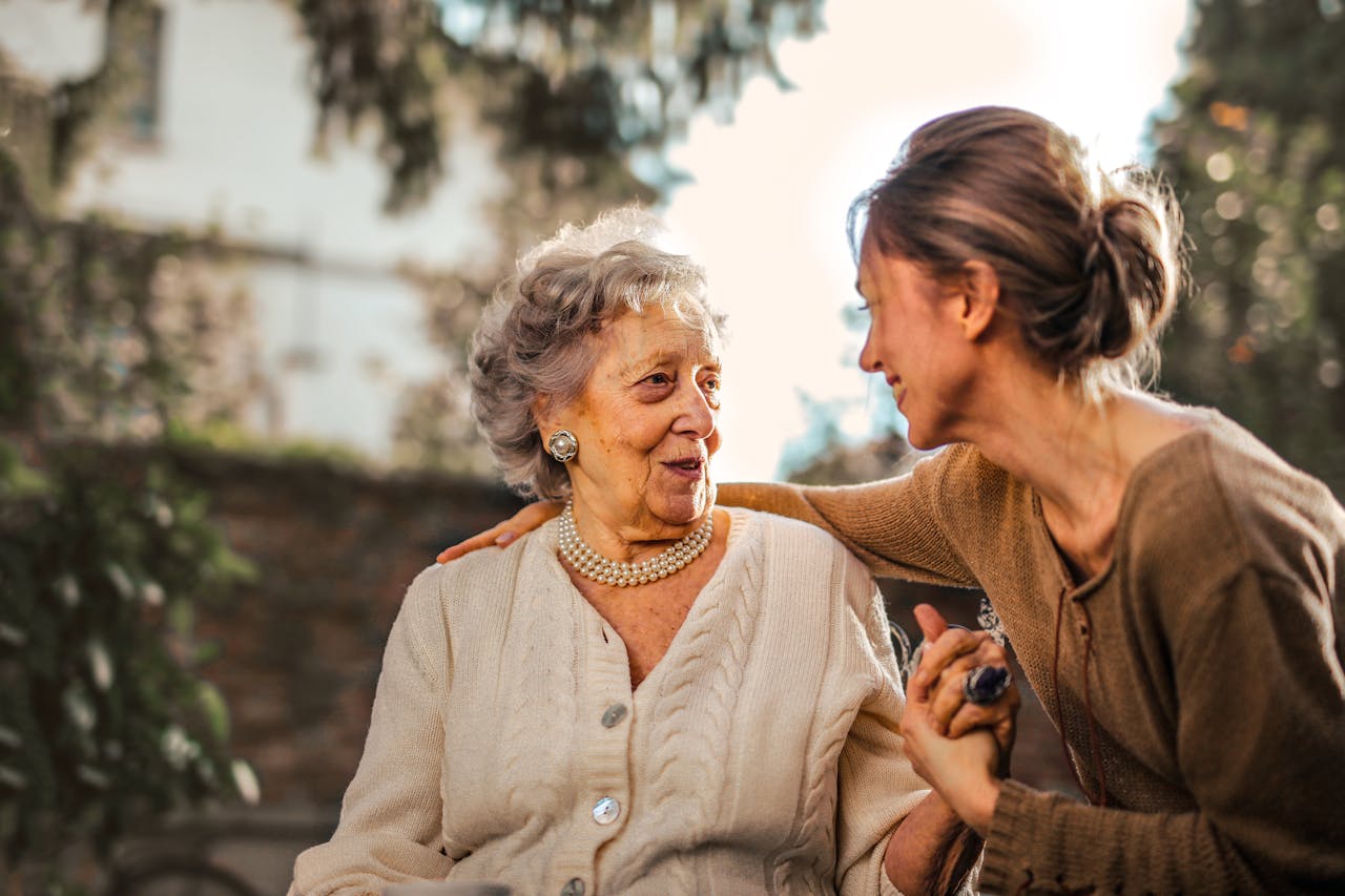 gallery-05 Elderly woman and adult daughter share a joyful, affectionate moment in a sunny garden.